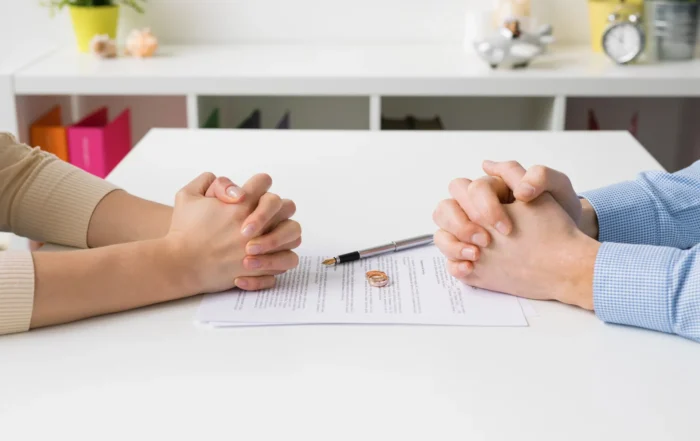 Separated couple with hands folded on either side of a separation agreement and wedding ring