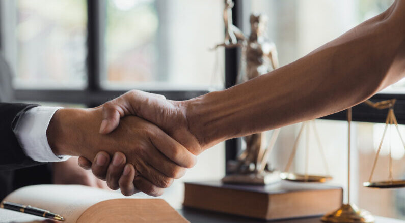 barrie-lawyer-client-handshake Two arms extended in a friendly handshake. The scales of justice in the background.